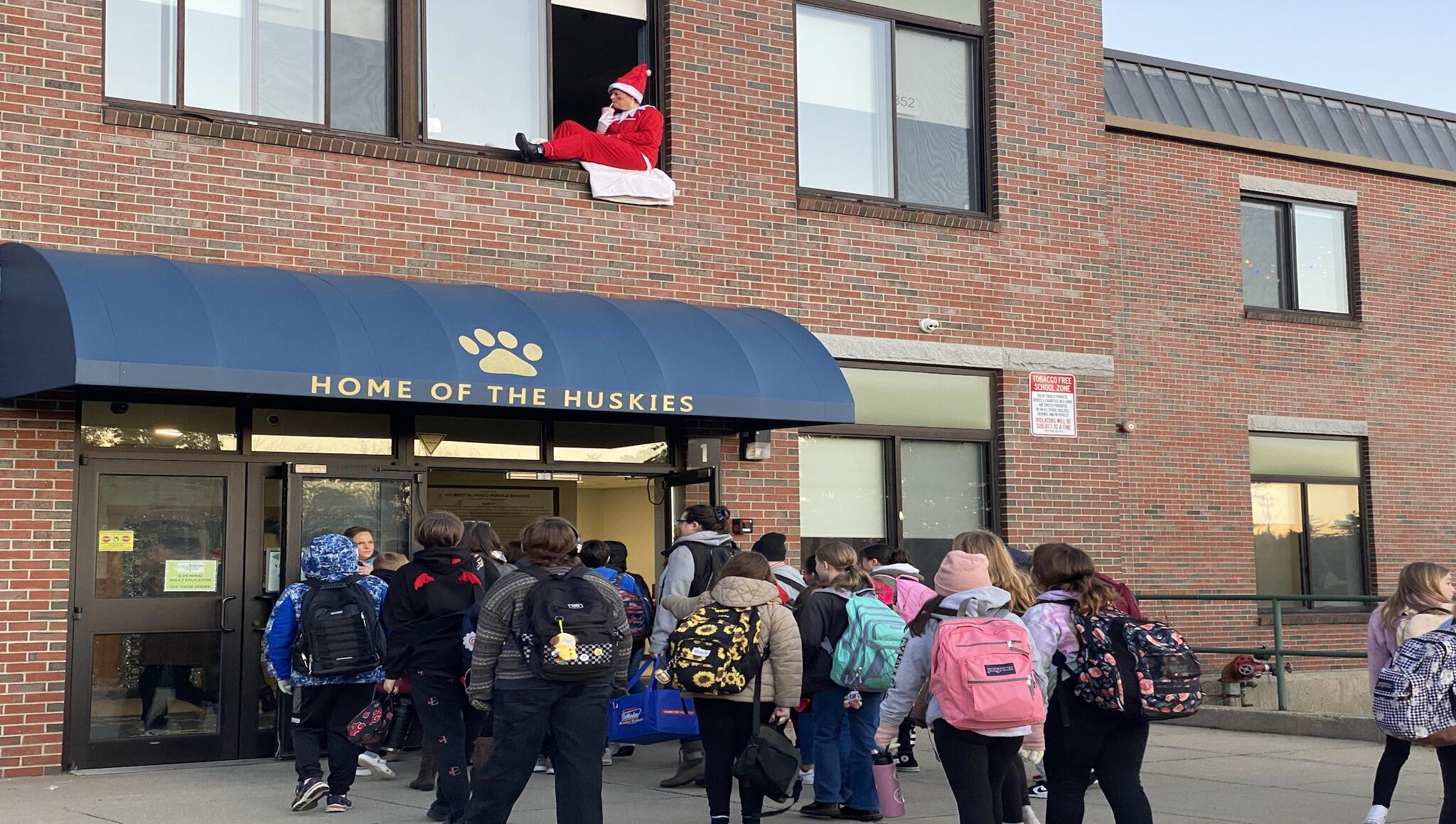 Students entering the school building with an elf sitting in the window above the door.