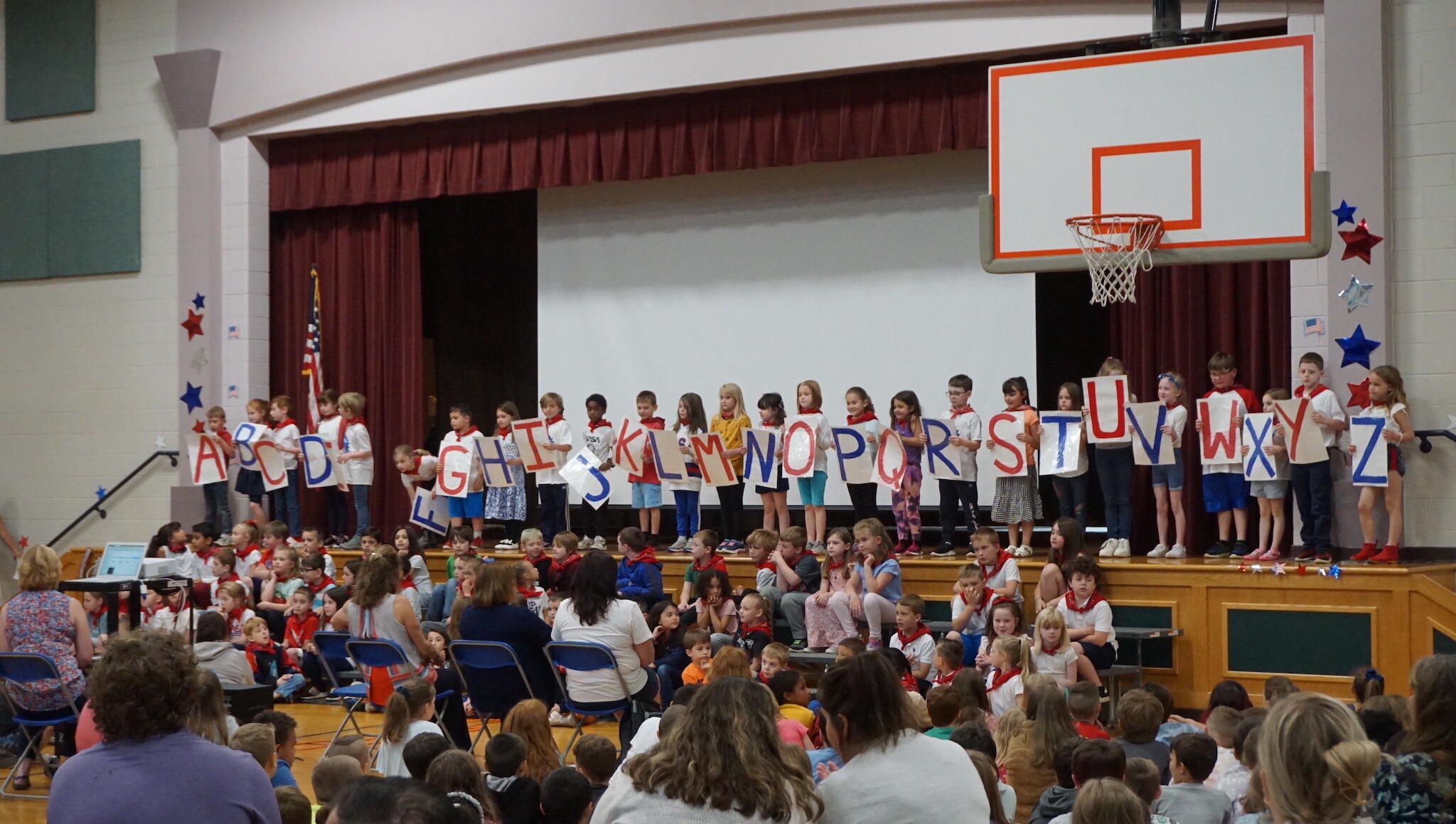 Students lined up across a school stage holding posters with letters of the alphabet.